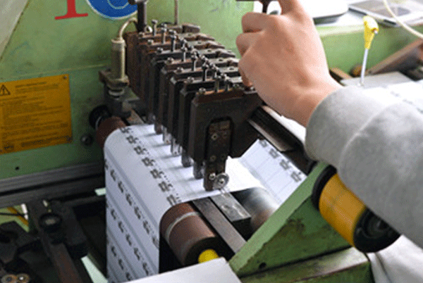 Operator setting up label production machine to ensure alignment and clean printing/weaving output