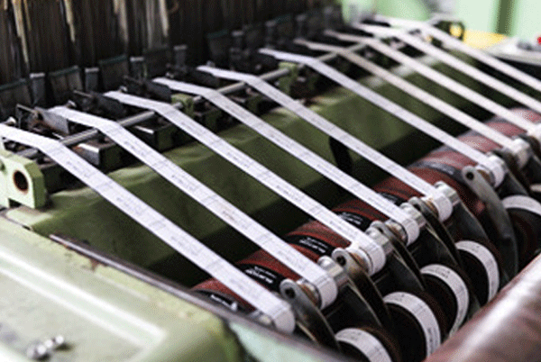 Woven label tapes running through finishing rollers for stable tension and consistent spacing